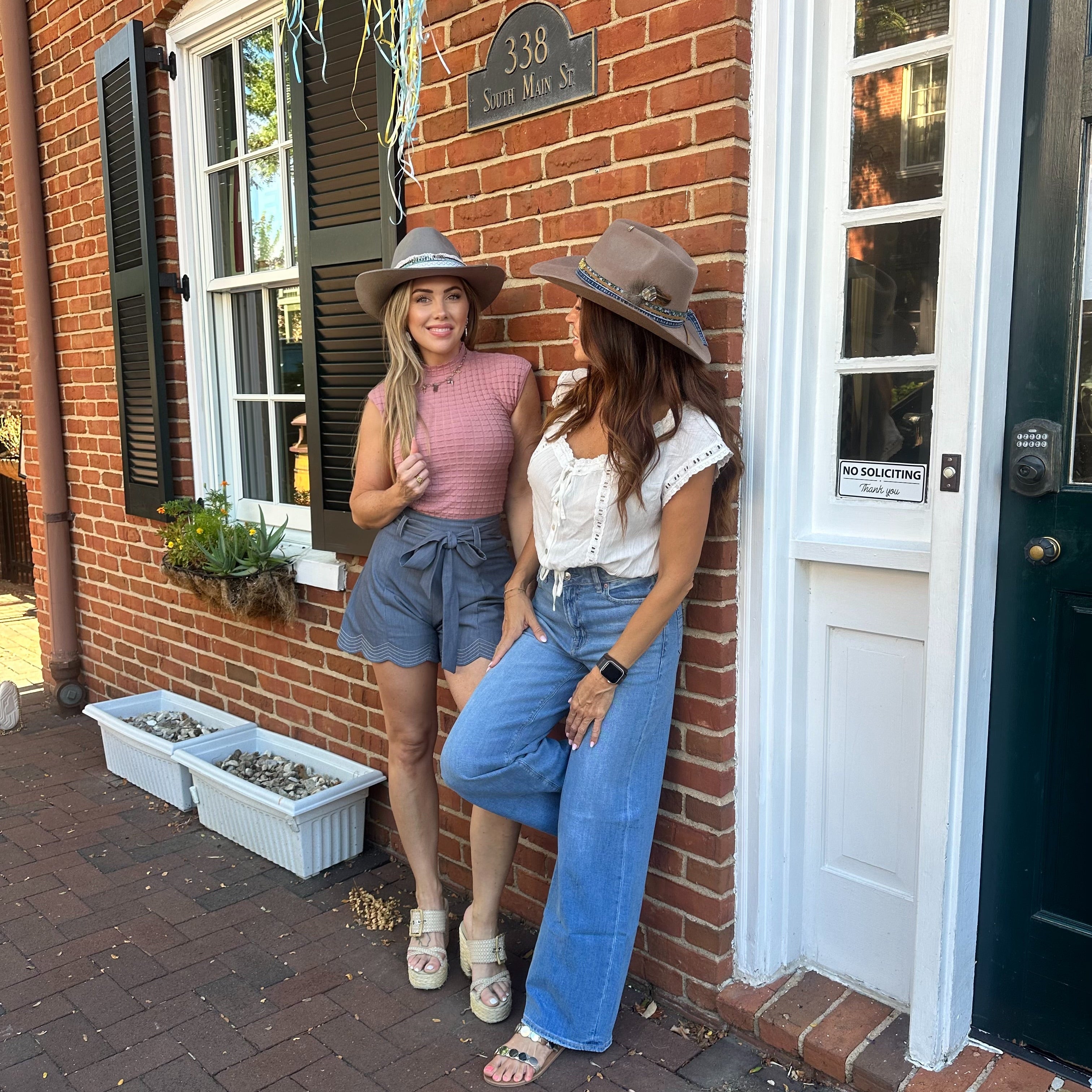Two women standing against a brick building, wearing hats and casual clothing.
